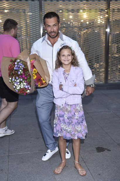 10-latka pozowała u boku taty. Miała na sobie różową sukienkę w kwiaty i jeansową kurtkę.  Marcin Łopucki trzymał w rękach 2 ogromne bukiety kwiatów.