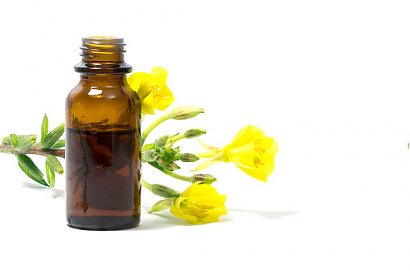 Olej z wiesiołka w buteleczce, a za nim żółte kwiaty